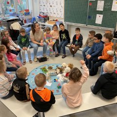 Children sit in a circle with a young woman