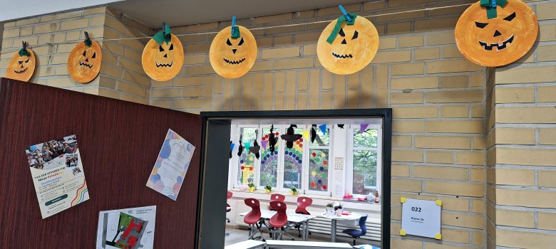 Visages d'Halloween bricolés sur une corde dans le couloir de l'école ; le spectateur peut regarder dans la salle de classe.