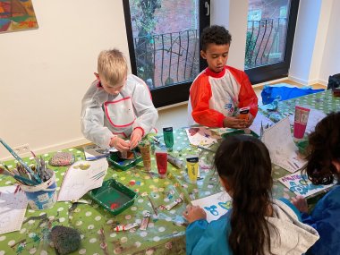 Kinderen in schilderpakjes schilderen met acrylverf en penselen